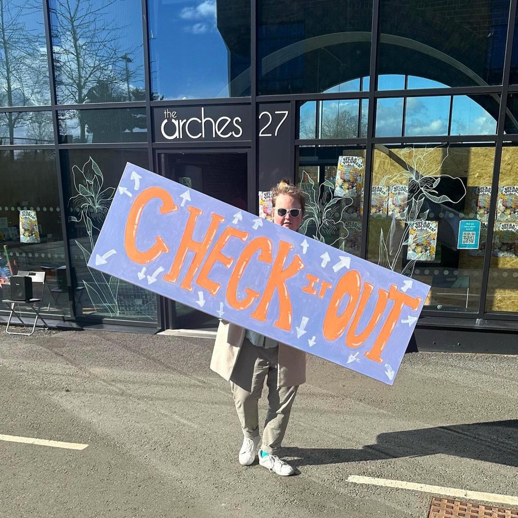 Tommy, a student, holds up a large canvas taht reads "Check it Out"