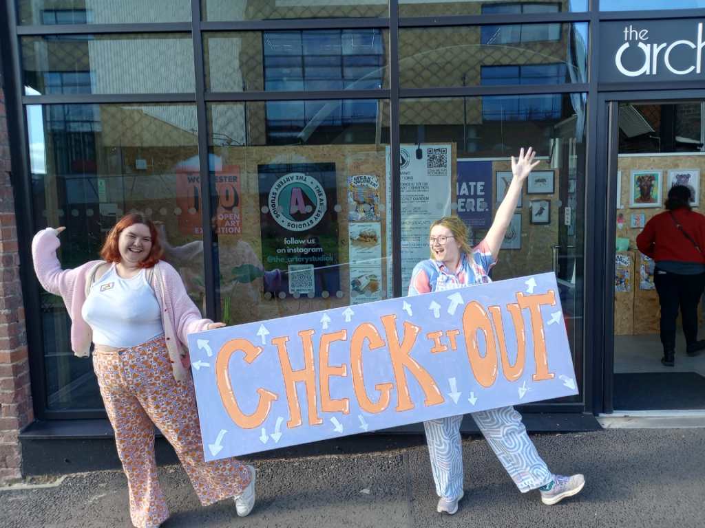 Directors Freddie and Lucy hold a large canvas and their hands in the air.
