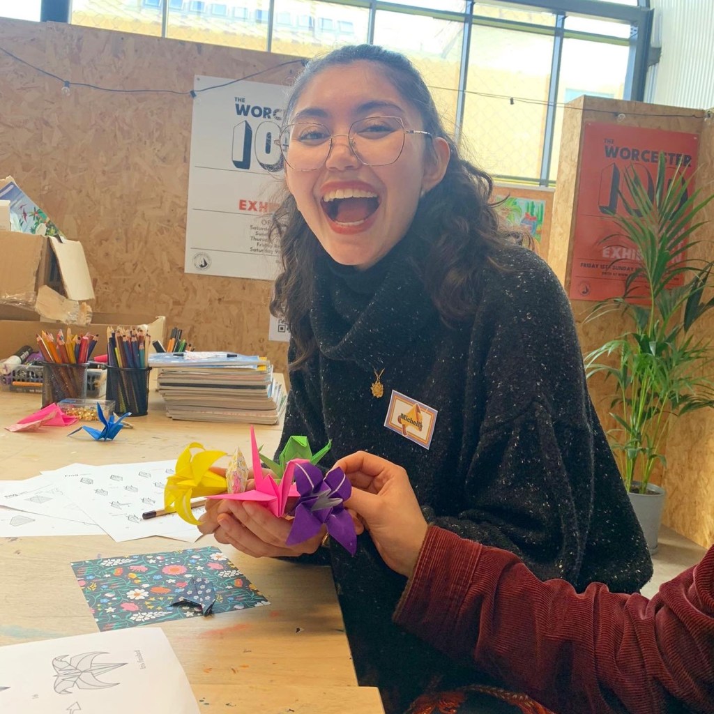 Michelle, a university student, holds her origami creation and smiles at the camera.