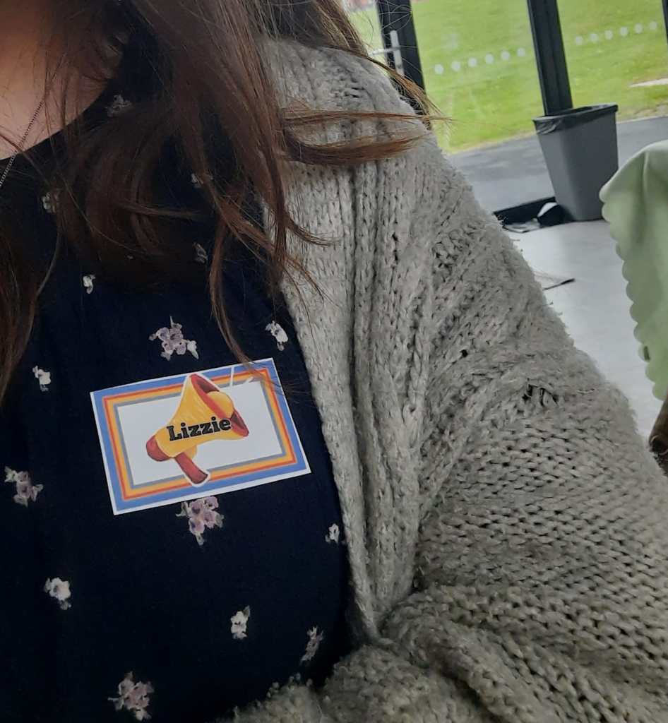 A custom volunteer name badge for Lizzie, with festival logo and colours.