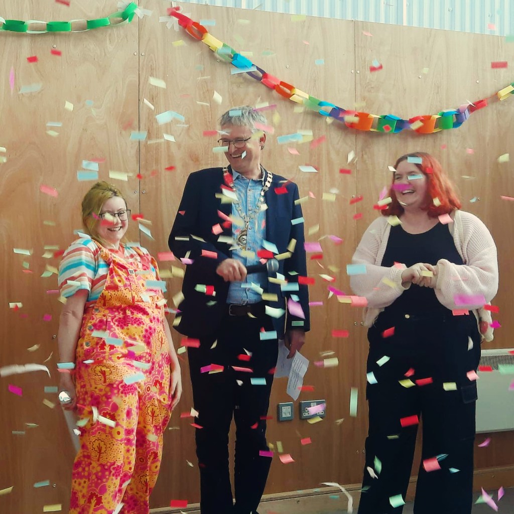 Festival directors, Freddie and Lucy, stand beside the Mayor of Worcester. They are surrounded by rainbow confetti.