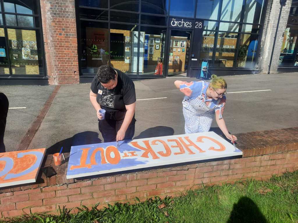 Two students paint letters onto a canvas.