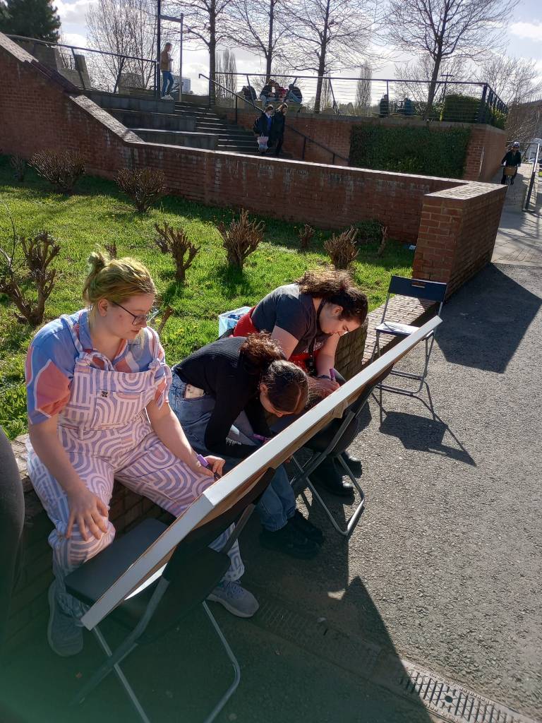 Four students painting a large canvas in the sun.