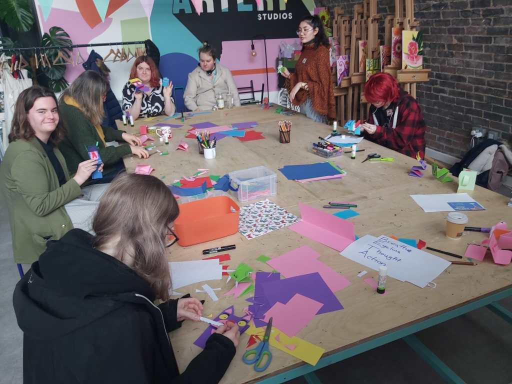A large workshop table with young people creating characters using colourful card and paper.